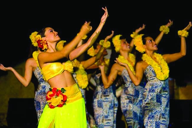 women dressed in traditional luau attire dancing with arms outstretched