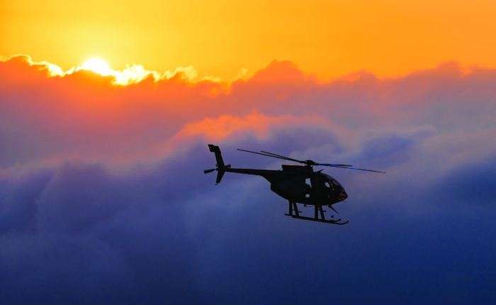 helicopter silhouetted against clouds and sun in the background