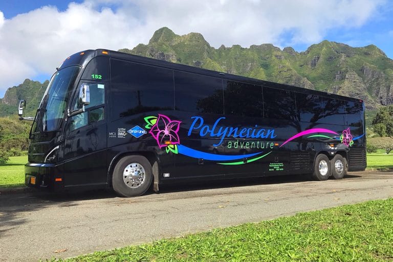 Large polynesian adventure Charter Bus Black parked in front of hawaiian mountain range